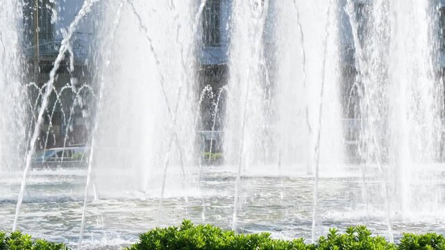 Clear sparkling water jets spray upward from a vibrant fountain in Omonia square, Athens, Greece. The blurred urban background highlights the dynamic movement and sunlight reflection. No people