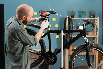 Bearded cyclist in casual clothes repairing bicycle fixing seat standing at home. Bicycle...