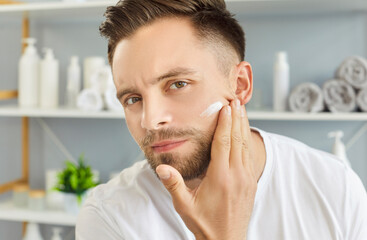 Man applying cream to face skin for healthy bathroom routine and skincare. Fingers of male hand...