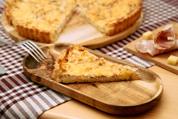 Savory quiche slice on wooden plate with ham and cheese garnish