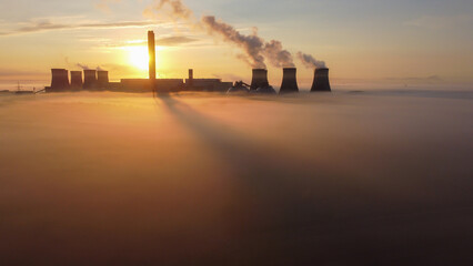 Aerial view of Drax Power Station enveloped in fog during sunrise, with smoke plumes rising from...