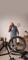 retired man making call while working with bike in home workshop. vertical banner