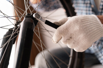 Close up of male hand carrying bike wheel maintenance indoors. checking wheel with wrench in home