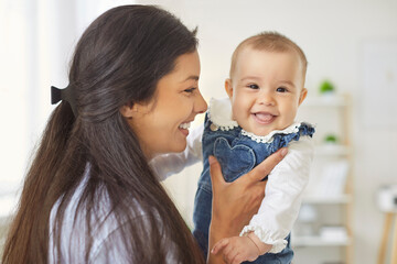 Mother holding newborn baby in arms, happy hugs of mom and cute smiling child in bedroom or nursery...