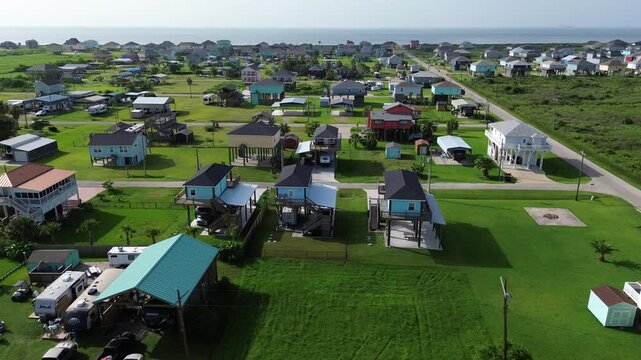 Long sandy shoreline of Beach Boyt in Port Bolivar, Texas with dense RVs parked beside colorful raised beach houses, bustling vacation zone, high seasonal demand, open layout with maintained lawn