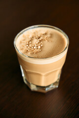 Velvety peanut butter latte in faceted glass on dark wooden table