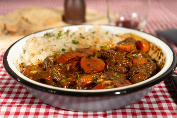 Hearty beef stew with carrots and rice on checkered tablecloth
