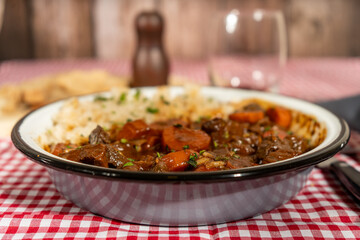 Delicious beef stew with carrots and rice served in enamelware on checkered tablecloth