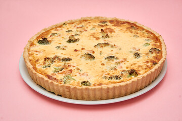 Delicious broccoli quiche on plate against soft pink backdrop