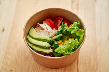 Fresh healthy salad bowl with grilled chicken, avocado, and vegetables on wooden table
