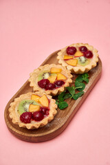 Delectable fruit tarts with fresh kiwi and berries on wooden tray
