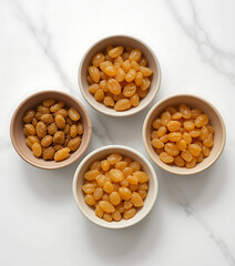  Set of five circular ceramic bowls in neutral tones, arranged in a fan shape, each filled with a different quantity of golden raisins. Clean white background emphasizes tonal harmony.

