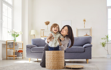 Happy mother and baby, woman, young child playing together in modern living room, nanny laughing,...