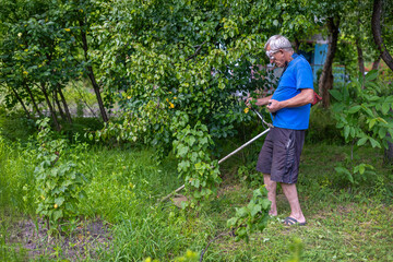 Senior man trimming garden grass with trimmer. An elderly man in casual clothes using an electric...