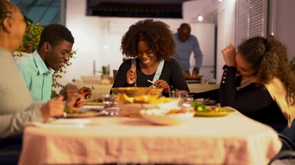 Happy african family eating dinner together at home patio - Black parents and children enjoy meal during night time outdoor - Powered by Adobe