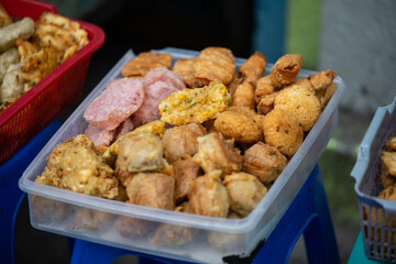 A clear container filled with various Indonesian fried snacks (