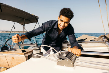 Young man maneuvering winch of a sailboat on a sunny summer day