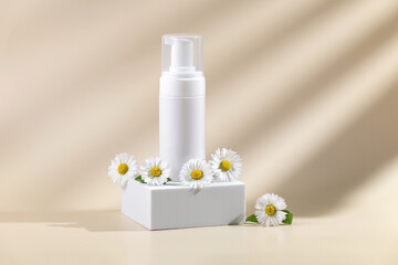 container with skin care products on a white square podium and daisy flowers on a beige background...