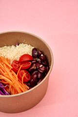 Healthy mediterranean bowl with couscous, cherry tomatoes, kidney beans, and carrot on pink background