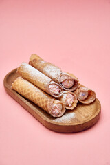 Delicious waffle cannoli pastries filled with cream and topped with pink sprinkles on wooden plate