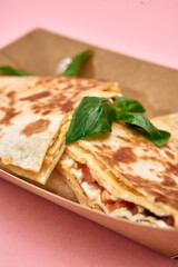 Delicious cheese tomato quesadilla with basil on cardboard plate against pink background