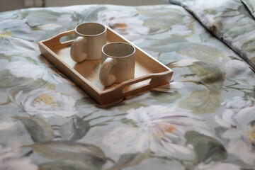 Cozy Morning in Bed with Floral Blanket and Two Mugs on Tray. Floral blanket and a wooden tray holding two ceramic mugs, perfect for coffee, tea, or a quiet moment shared. 