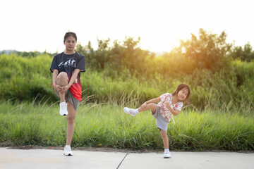 Mother and daughter are exercising in the park with joyful. Nature and sunset are background. A child is doing physical exercises as her mother teaches her.