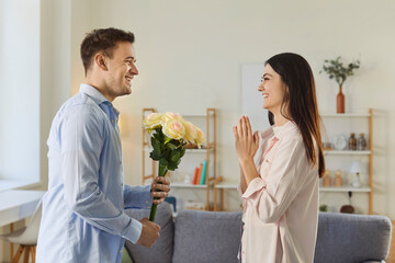 Young cheerful man congratulating on holiday happy girlfriend with bouquet of flowers. Smiling...