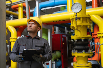 Asian engineer wearing glasses working in the boiler room,maintenance checking technical data of...