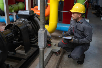 Asian engineer wearing glasses working in the boiler room,maintenance checking technical data of...