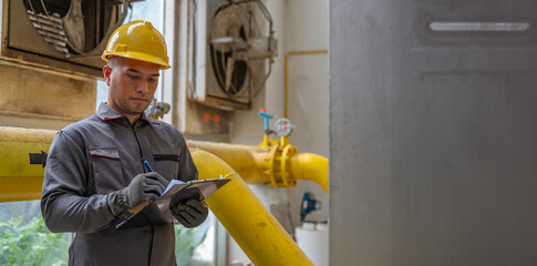Asian engineer wearing glasses working in the boiler room,maintenance checking technical data of...