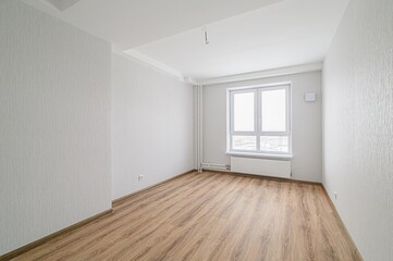 empty, bright room features wood-like flooring, light textured wallpaper, a white window with a...
