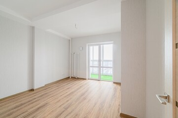 bright, empty room with wood floors and white walls. A balcony is visible through the window