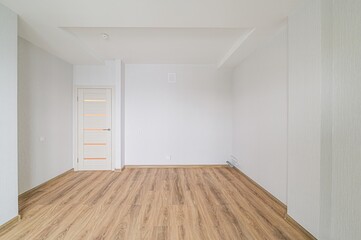 bright, empty room with wood-like flooring, white walls, and a white door with horizontal glass panes, creating a clean and minimalist aesthetic