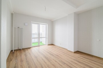 Bright, empty room with wood floors, white walls, a radiator, and a balcony door. Minimalistic
