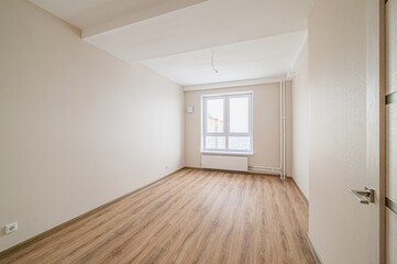 empty, bright room with wooden floors, beige walls, and a window letting in natural light