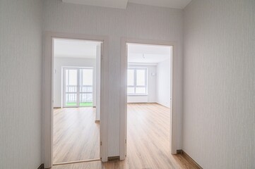 Bright hallway with two open doorways leading to rooms with wood floors and windows. The walls are...
