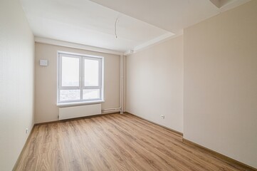 bright, empty room with wood flooring, light beige walls, and a large white window. A radiator sits...