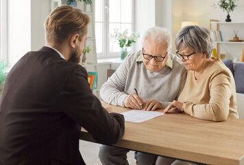 Confident gray-haired elderly senior couple sitting at the desk in office with a young man advisor...