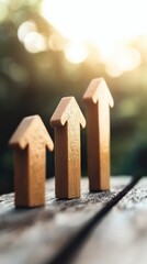 Three wooden arrow figures of increasing height symbolize growth and progress on a blurred natural background with sunlight.