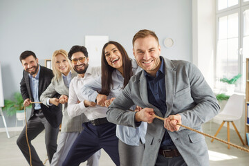 Cheerful multicultural business team playing tug of war together in office. Smiling colleagues...