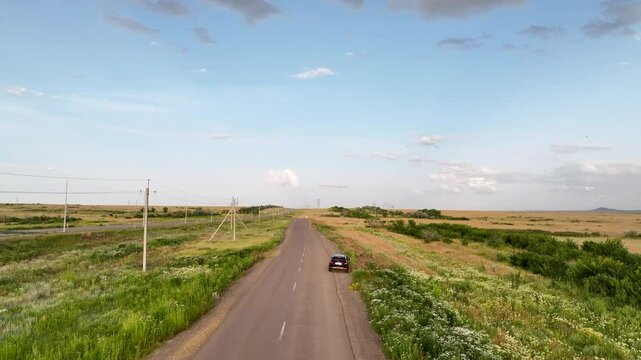 Drone video of a black car pulling over on the side of a dirt road in the vast open steppe, capturing solitude, travel and the natural landscape from above.