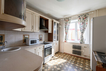 cozy kitchen with cream-colored cabinets, tiled backsplash, patterned floor, and a window with floral curtains