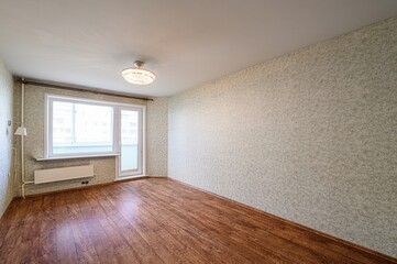 Bright, empty room with wood floor, patterned wallpaper, a window with radiator, and a ceiling light