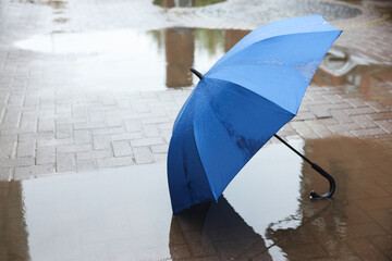 Blue umbrella on wet asphalt outdoors, space for text
