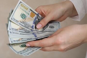 Woman counting dollar banknotes on beige background, closeup