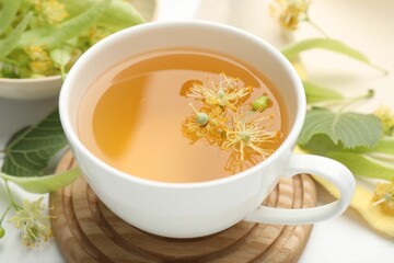 Fresh linden tea in cup and flowers on white table, closeup