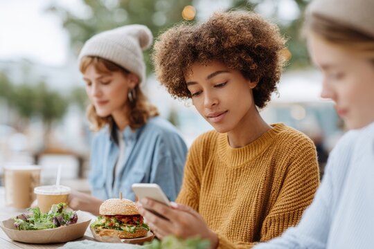 Friends enjoying lunch outdoors while one checks her phone in a casual dining setting