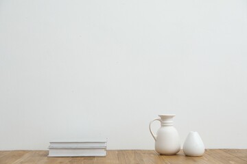 Different vases and books on wooden table near white wall indoors