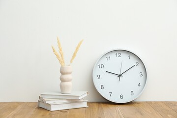 Dried spikes, books and round clock on wooden table near white wall indoors